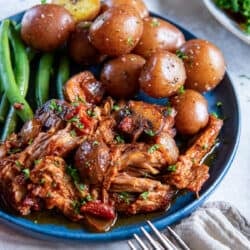 Italian pork roast on a blue plate with parsley potatoes and green beans.