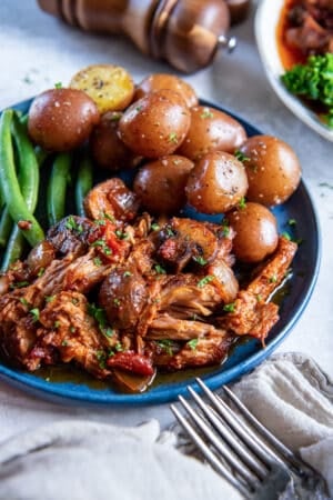 Italian pork roast on a blue plate with parsley potatoes and green beans.