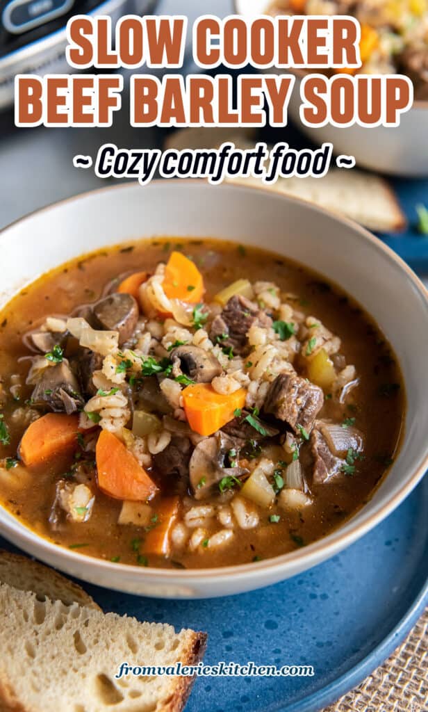 A bowl of beef barley soup on a blue plate with toasted bread with text.