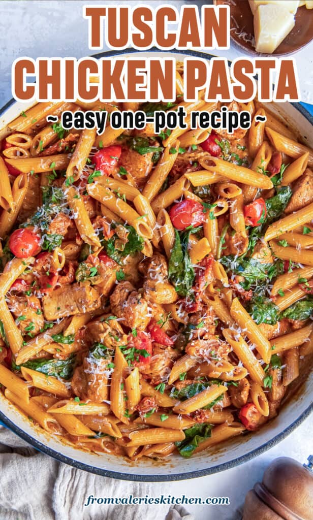A skillet full of pasta with chicken, sundried tomatoes, cherry tomatoes, and spinach next to a pepper grinder with text.