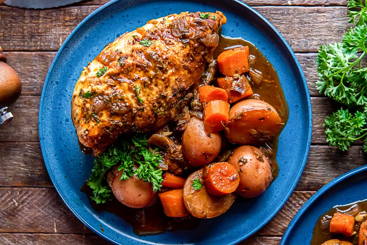 A serving of braised chicken with carrots and potatoes on a blue plate.