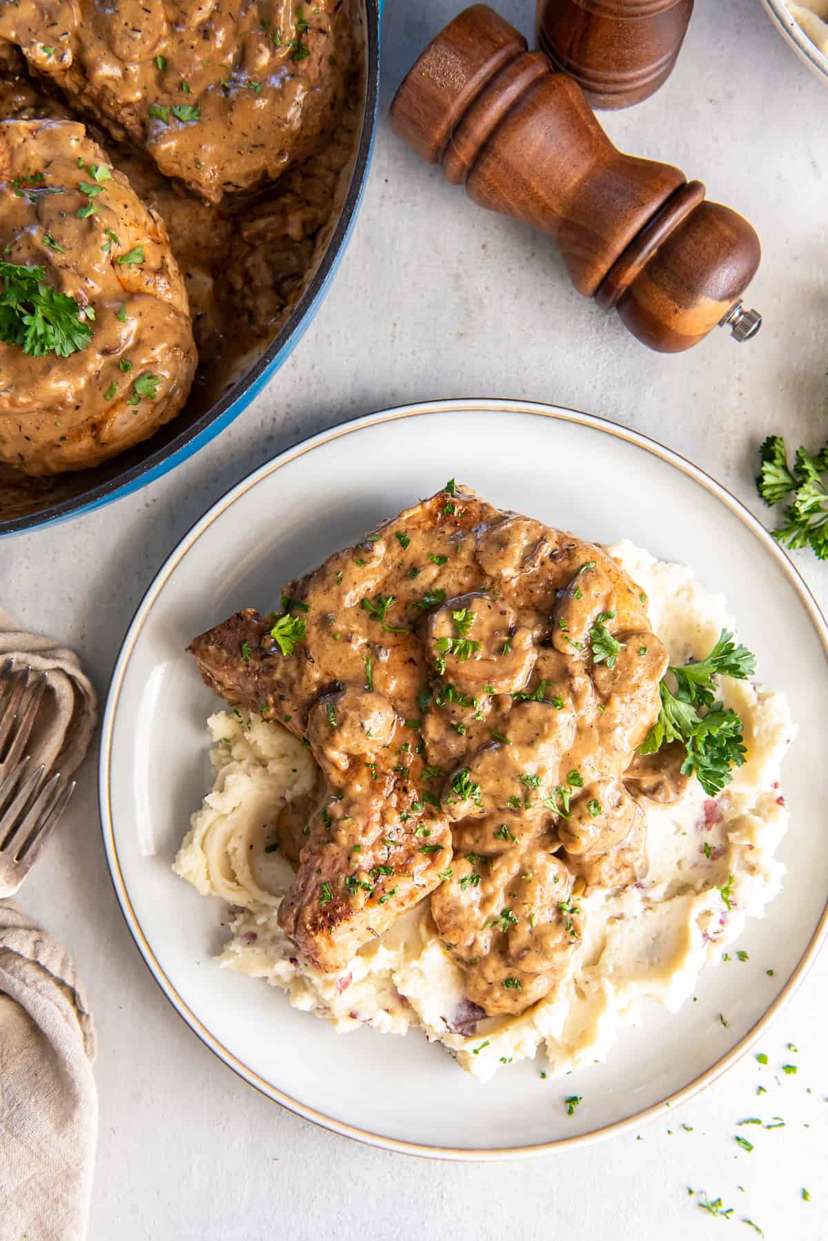 A pork chop topped with mushroom gravy over a mound of mashed potatoes on a dinner plate.