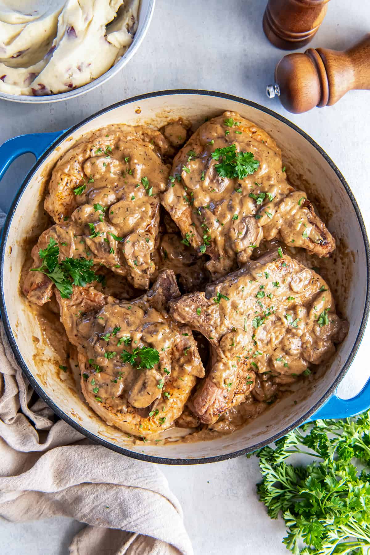 Four pork chops topped with cream of mushroom gravy in a skillet.