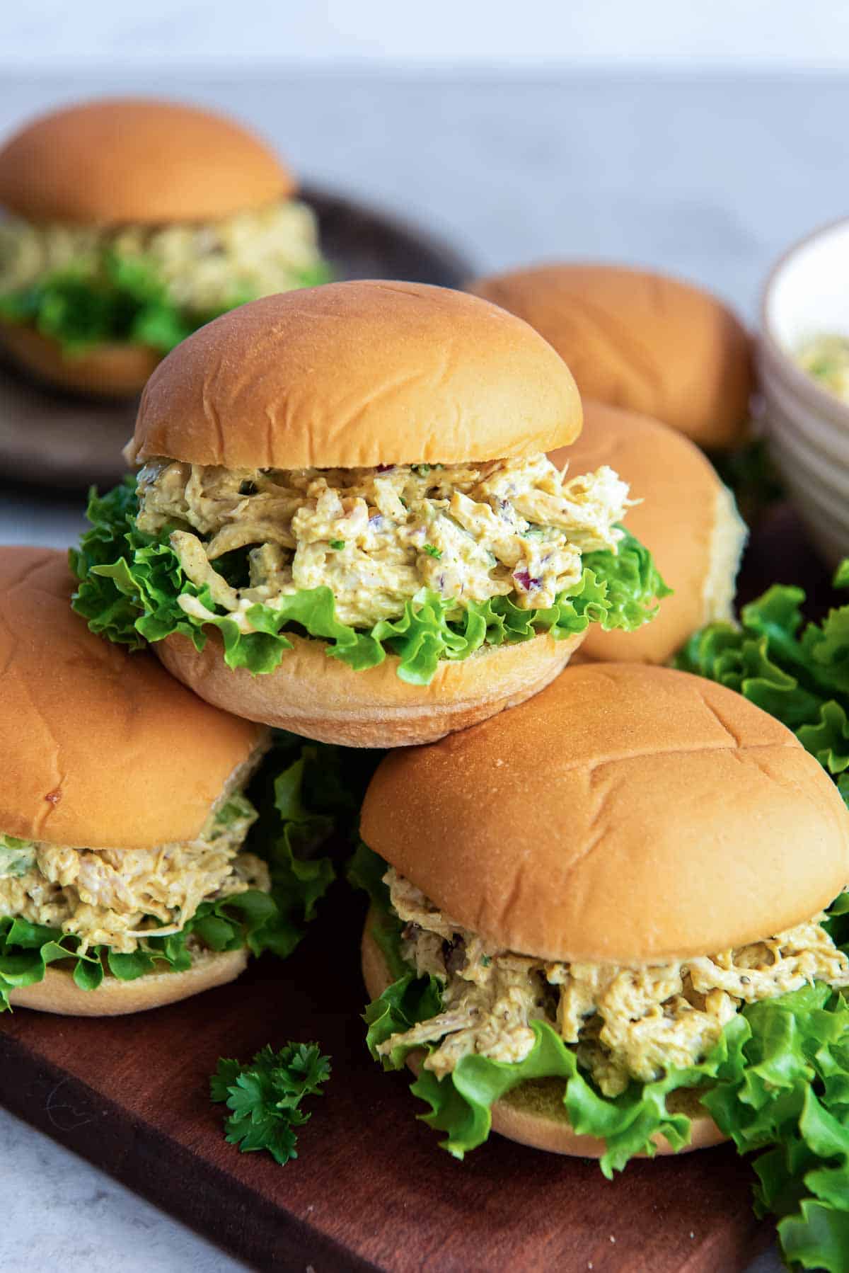 Curry chicken salad on slider rolls piled on a wood board.