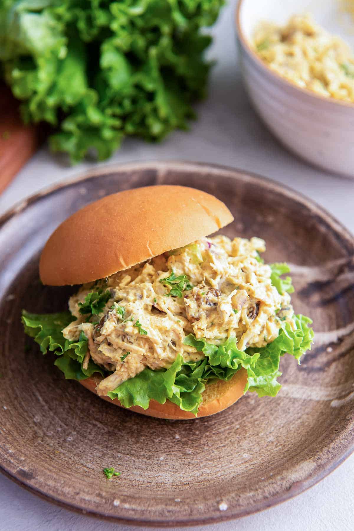 A small sandwich roll filled with curry chicken salad and lettuce on a wooden plate.