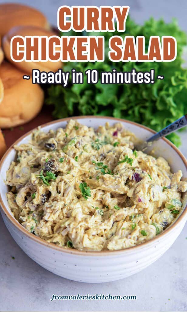 Curry chicken salad in a bowl with a spoon next to sandwich rolls and lettuce with text.