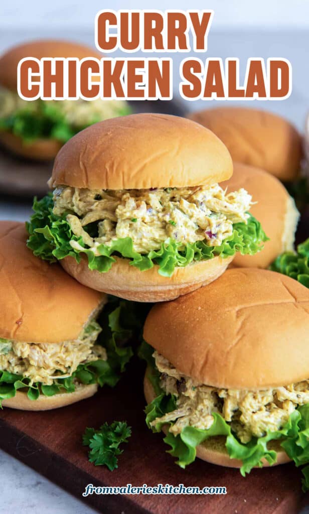 Curry chicken salad on slider rolls piled on a wood board with text.