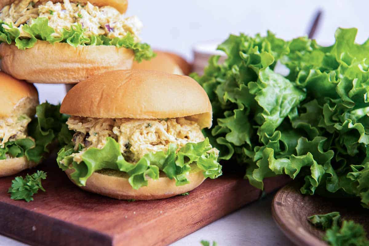 Curry chicken salad on slider rolls piled on a wood board.