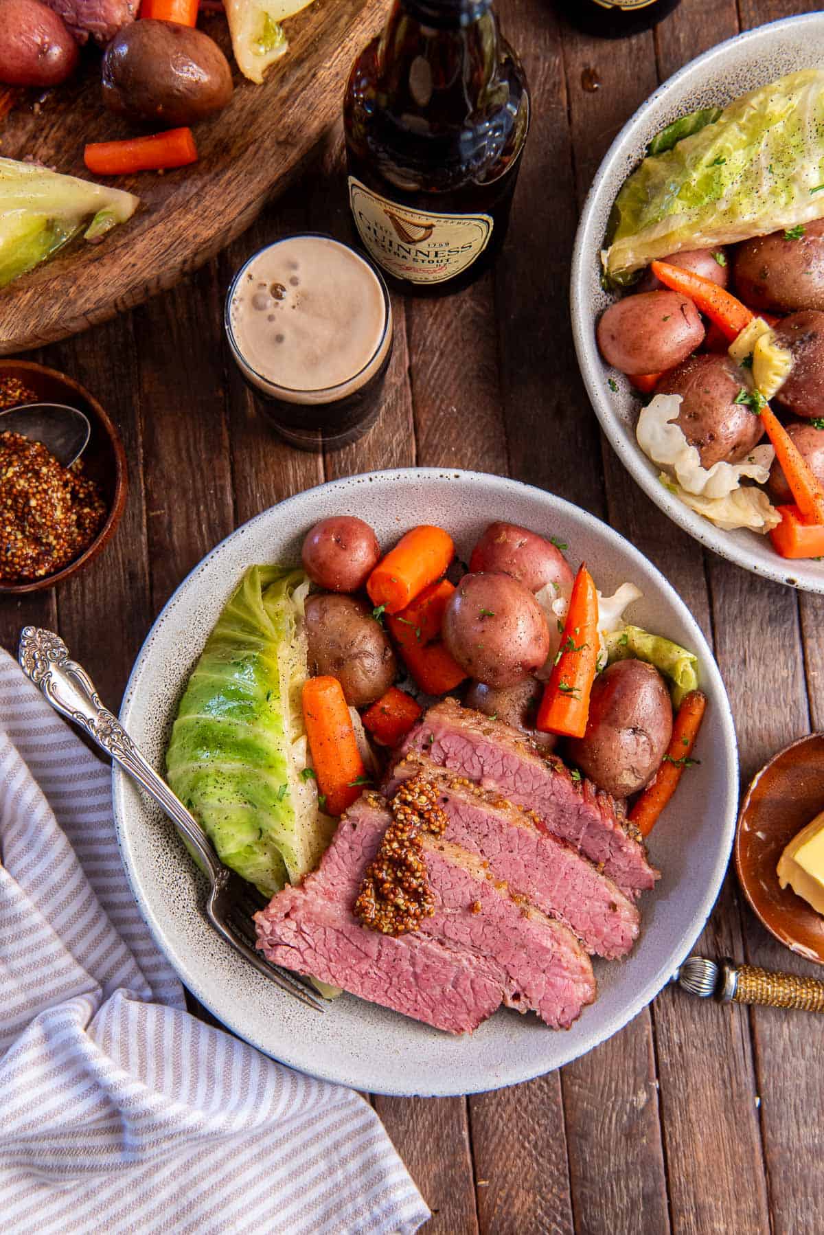 Two bowls of corned beef and cabbage with carrots and potatoes next to a glass filled with Guinness beer.