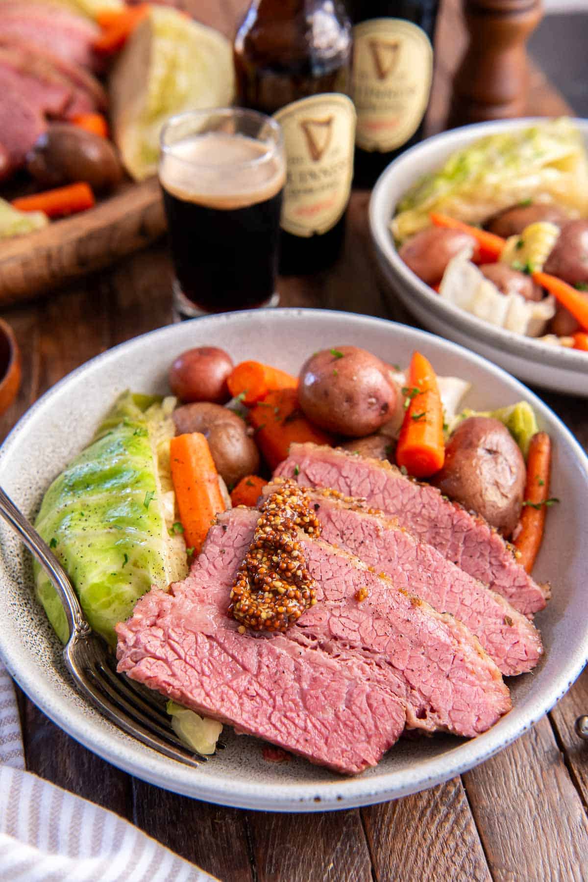 Slices of corned beef topped with a little stone ground mustard in a bowl in cabbage, carrots, and potatoes.