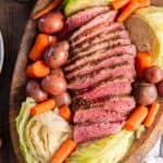 Sliced corned beef, cabbage, carrots, and potatoes on a wood platter.