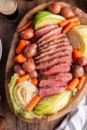 Sliced corned beef, cabbage, carrots, and potatoes on a wood platter.