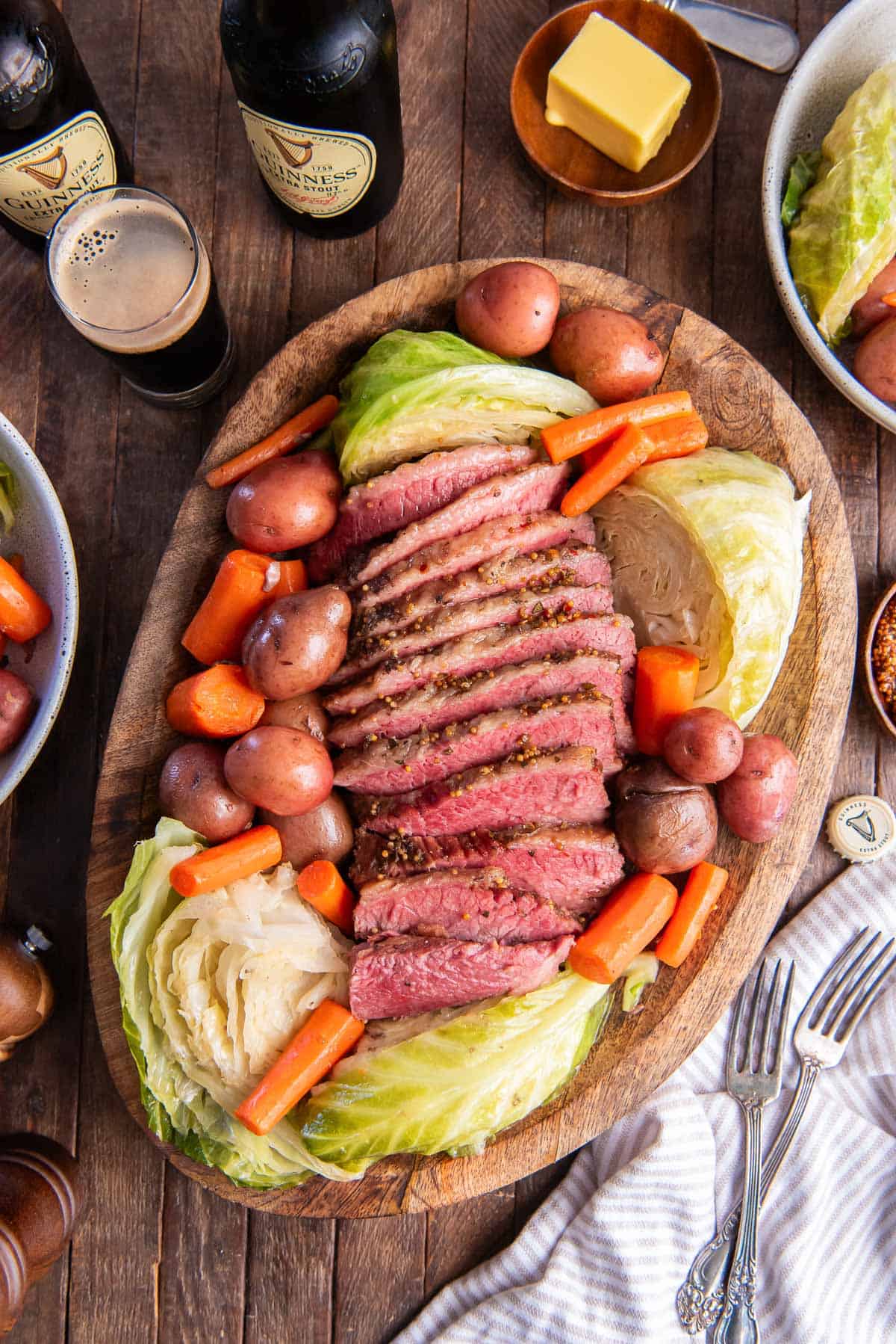Sliced corned beef, cabbage, carrots, and potatoes on a wood platter.