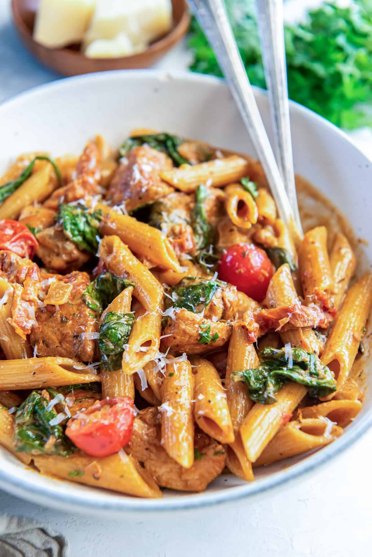 Forks resting in a bowl of tuscan chicken pasta.