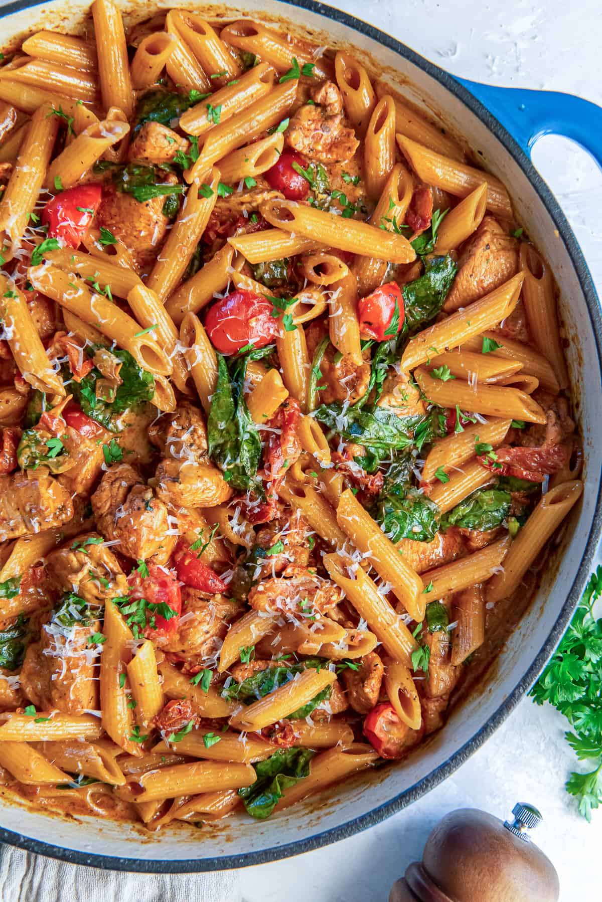 A skillet full of pasta with chicken, sundried tomatoes, cherry tomatoes, and spinach.