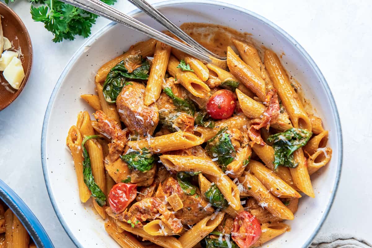 Forks resting in a bowl of tuscan chicken pasta.