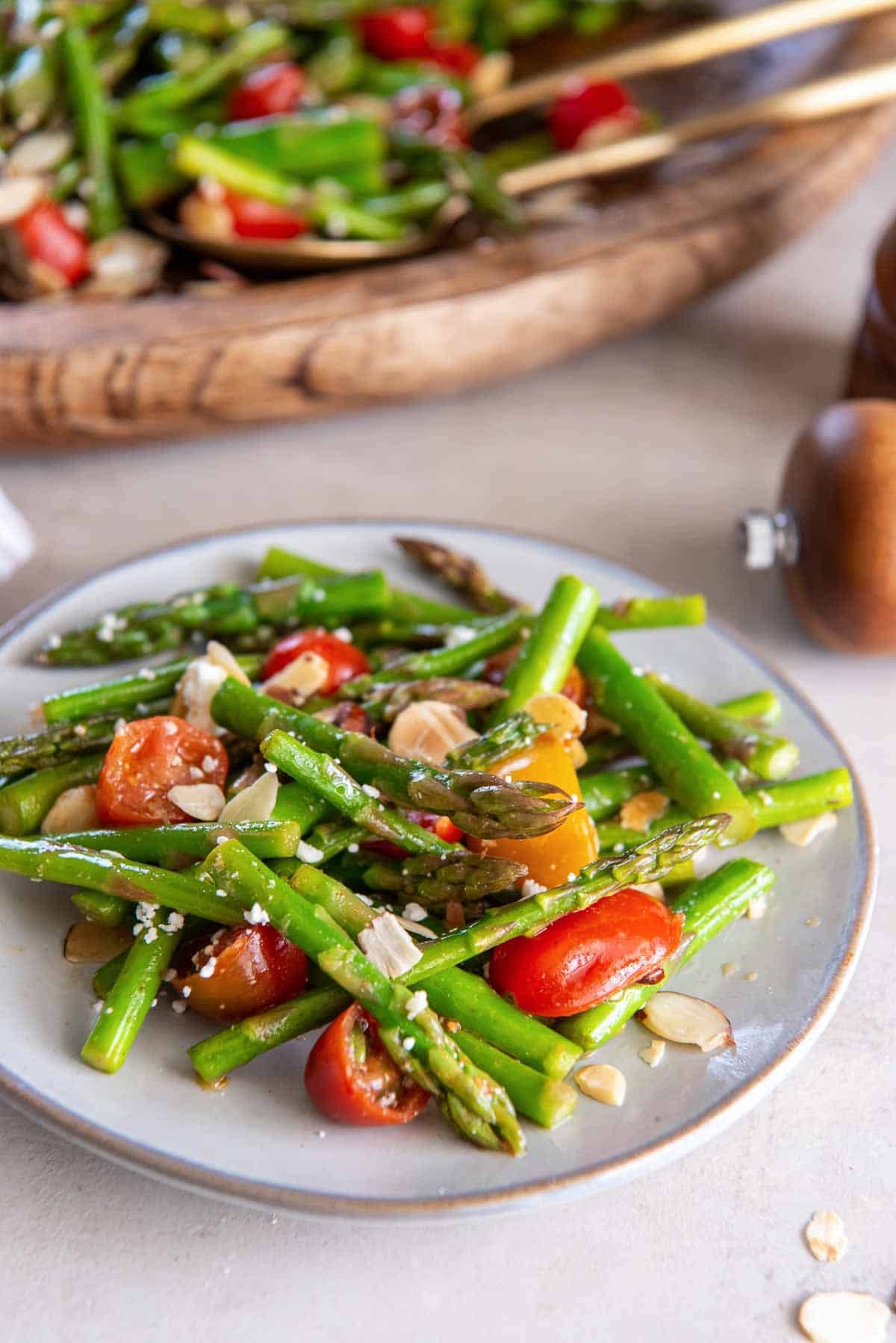 Asparagus salad with cherry tomatoes, almonds, and feta on a small white plate.