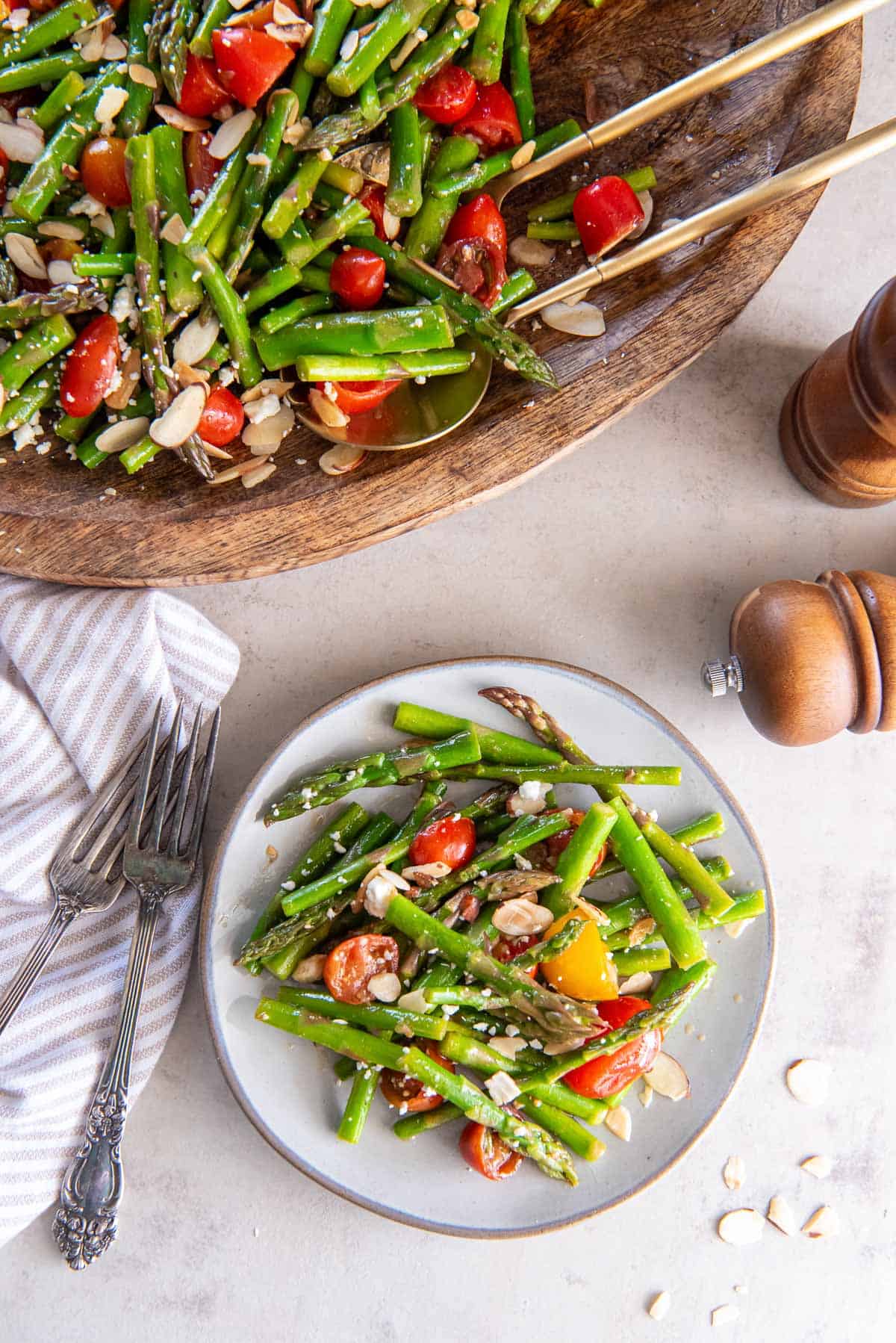 A large serving platter and small serving plate filled with asparagus salad.