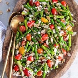 Asparagus salad with cherry tomatoes, almonds, and feta on a wood platter.