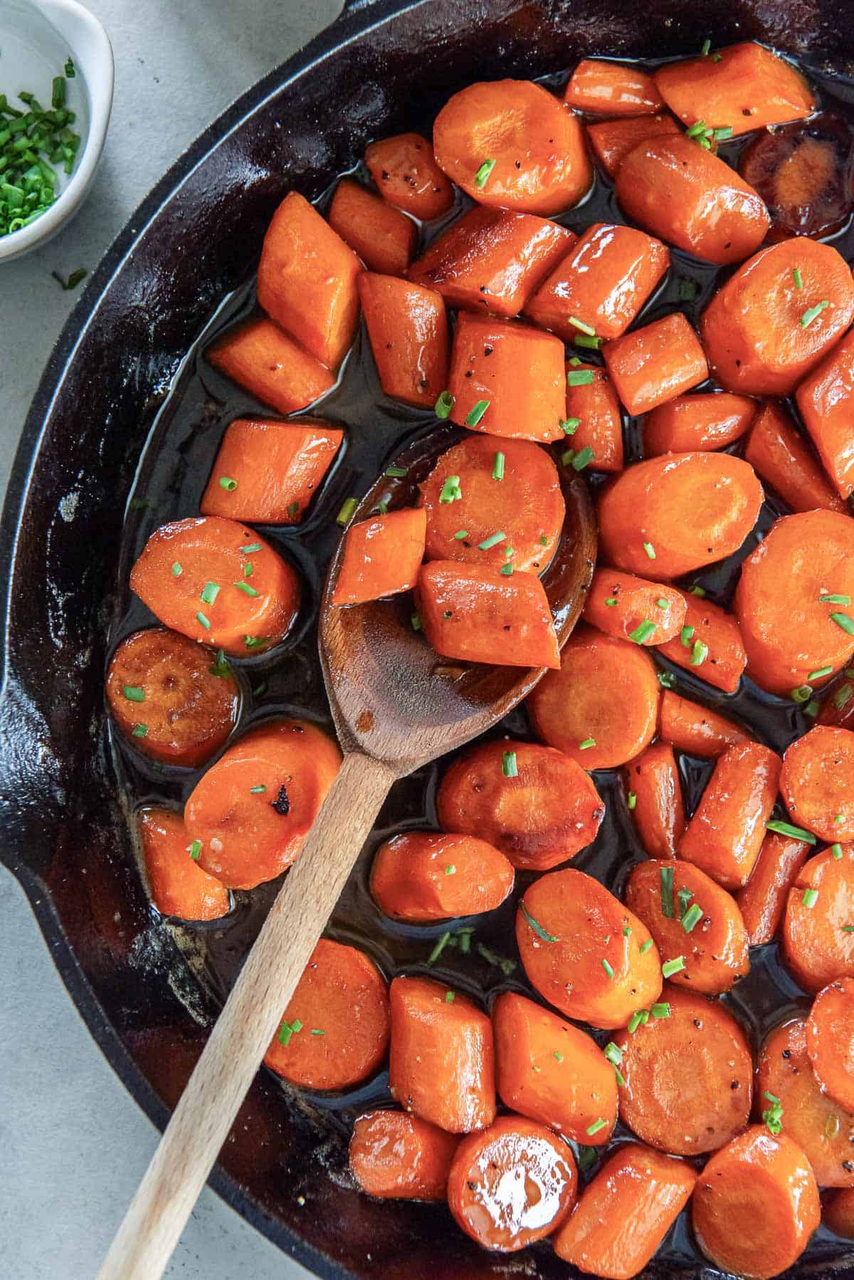 A wooden spoon resting in a cast iron skillet filled with bourbon glazed carrots.