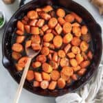 A wooden spoon resting in a cast iron skillet filled with bourbon glazed carrots.