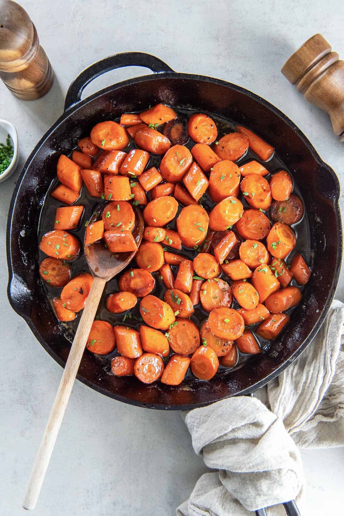 A wooden spoon resting in a cast iron skillet filled with bourbon glazed carrots.