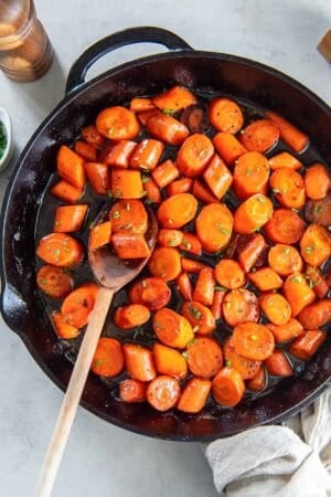 A wooden spoon resting in a cast iron skillet filled with bourbon glazed carrots.