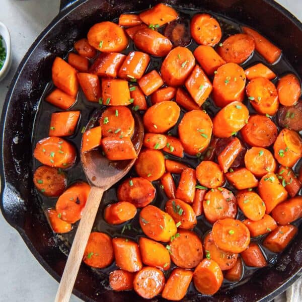 A wooden spoon resting in a cast iron skillet filled with bourbon glazed carrots.