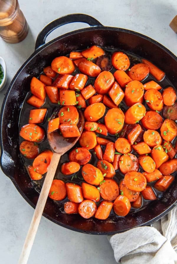 A wooden spoon resting in a cast iron skillet filled with bourbon glazed carrots.