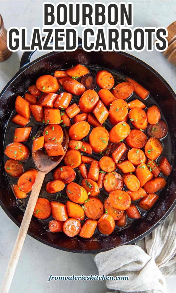 A wooden spoon resting in a cast iron skillet filled with bourbon glazed carrots with text.
