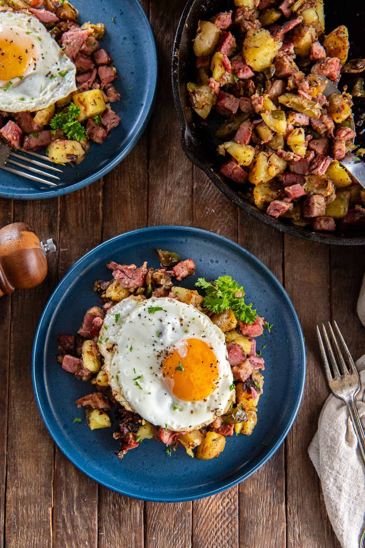 Corned beef hash on blue plates topped with fried eggs.