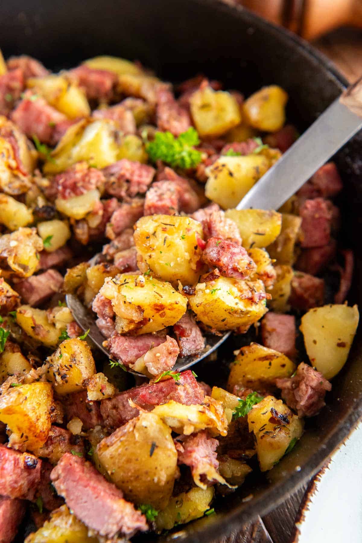 A spoon scooping corned beef hash from a cast iron skillet.