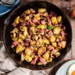 Corned beef hash in a cast iron skillet next to a plate of fried eggs.