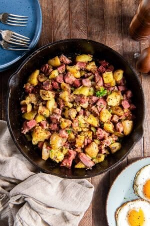 Corned beef hash in a cast iron skillet next to a plate of fried eggs.