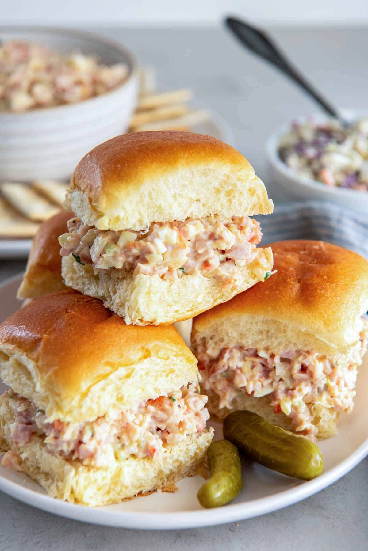 Ham salad on slider buns stacked on a plate with two pickles.