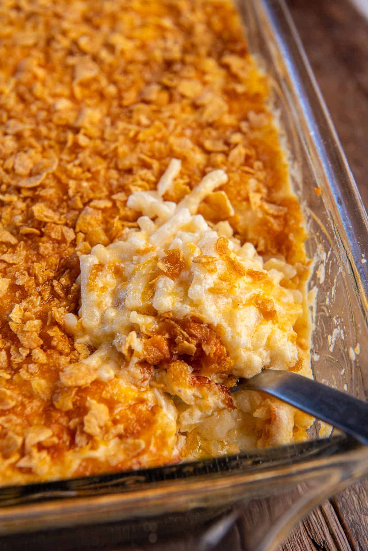 A spoon resting in cheesy hash brown casserole in a baking dish.