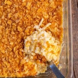 A spoon resting in cheesy hash brown casserole in a baking dish.