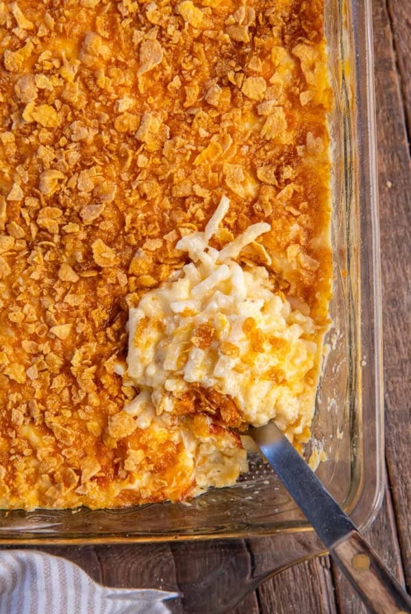 A spoon resting in cheesy hash brown casserole in a baking dish.