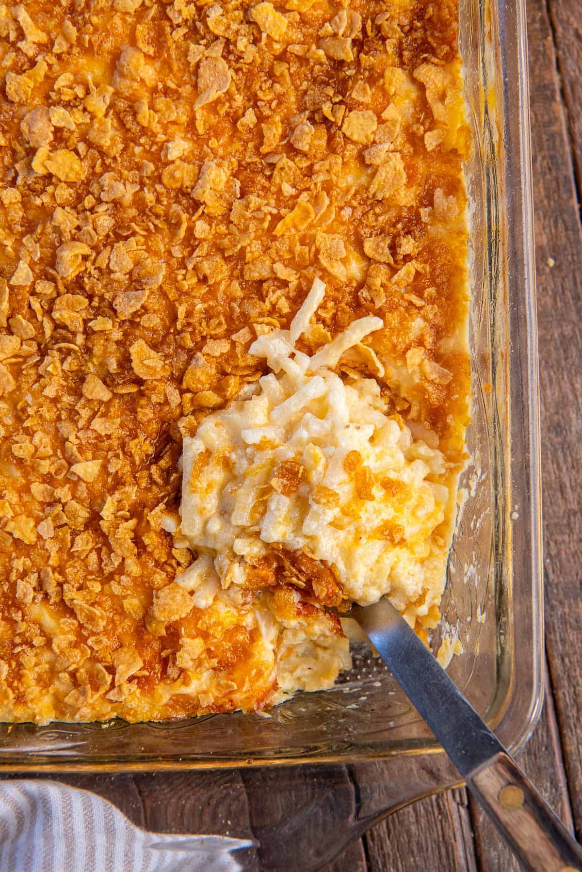 A spoon resting in cheesy hash brown casserole in a baking dish.