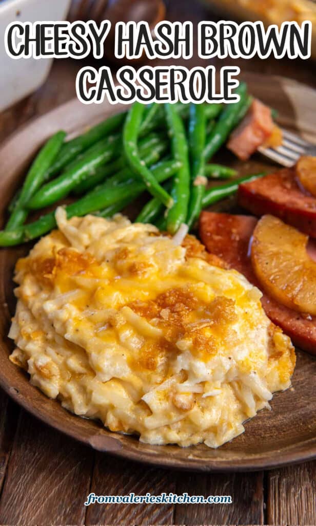 A serving of hash brown casserole on a brown plate with ham and green beans with text.