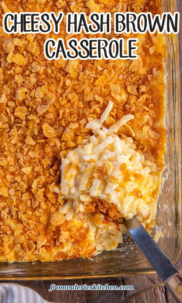 A spoon resting in cheesy hash brown casserole in a baking dish with text.