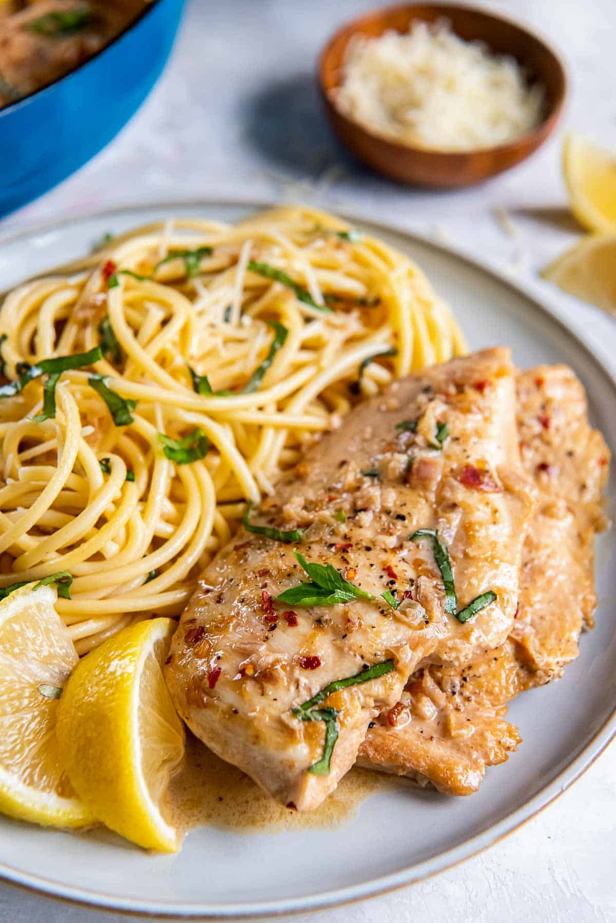 Lemon chicken and pasta on a plate witih lemon wedges.