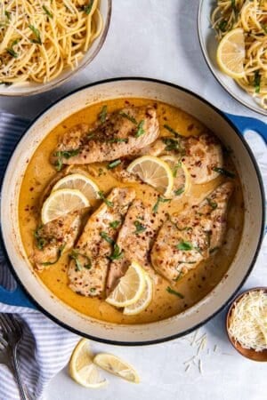 Chicken in a skillet with lemon cream sauce surrounded by bowls of pasta.