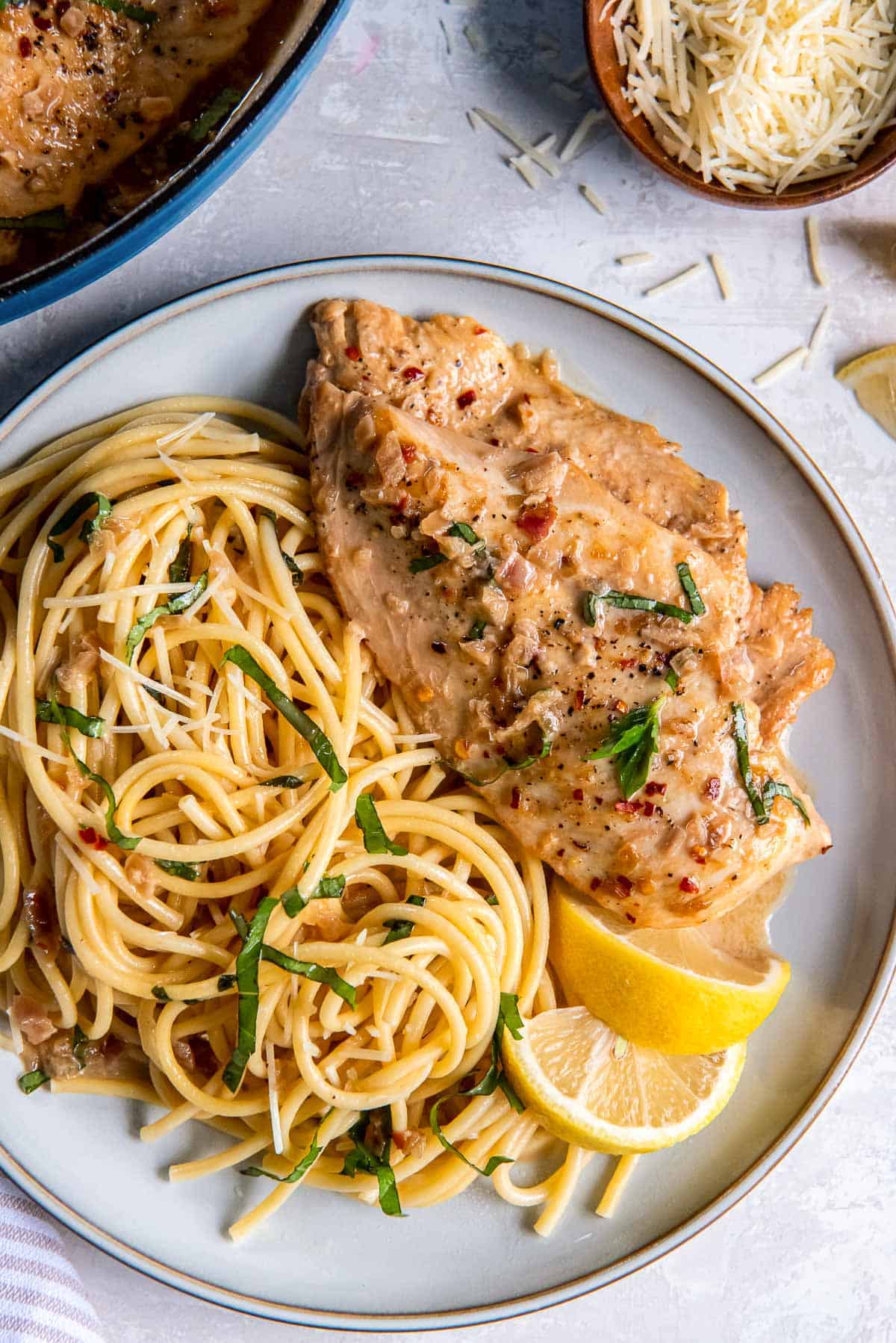 Lemon chicken and pasta on a plate witih lemon wedges.