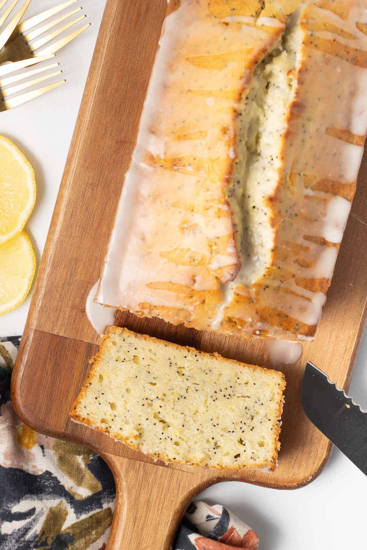 A loaf of glazed lemon poppy seed bread on a cutting board.