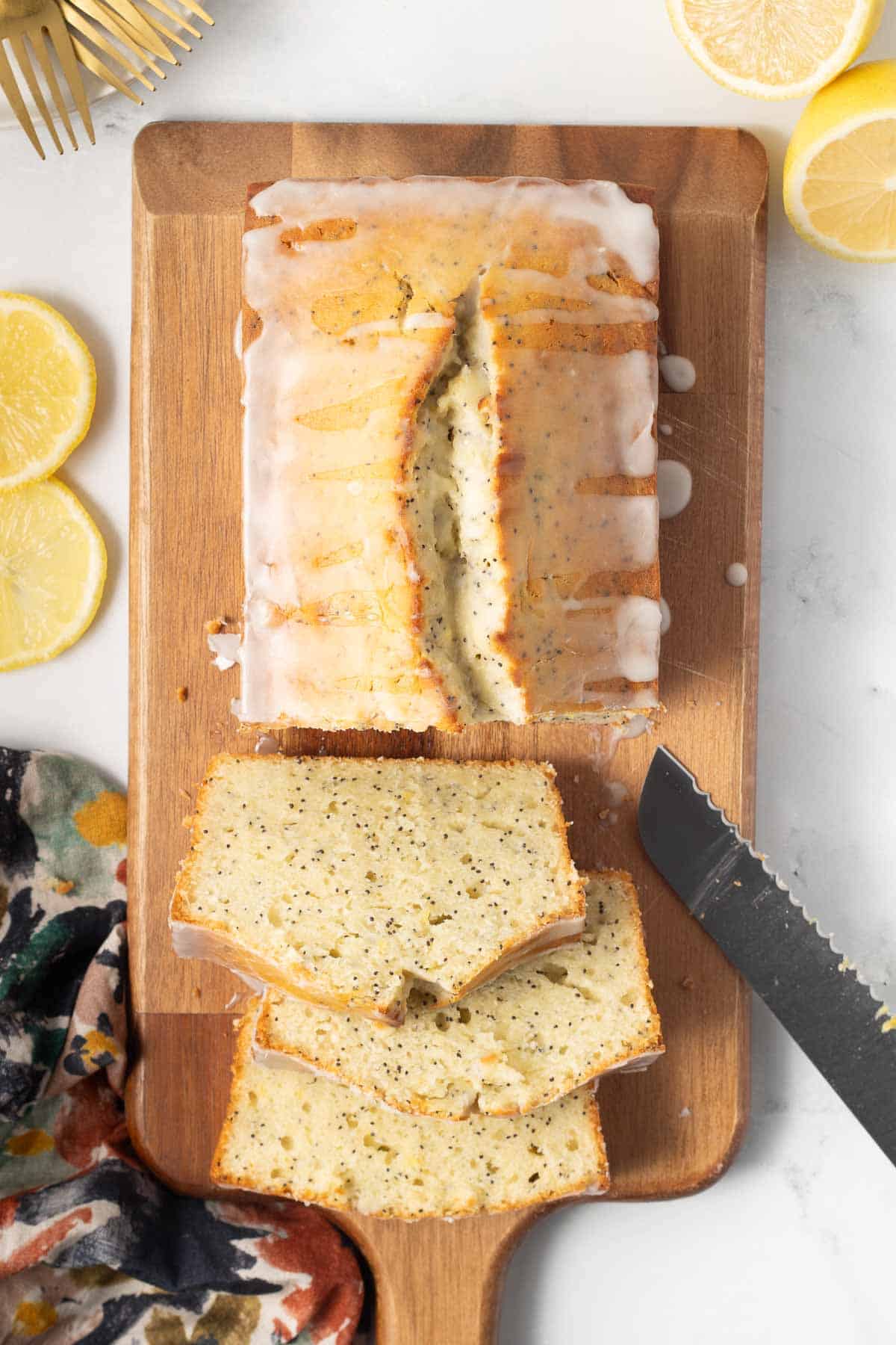 A sliced loaf of glazed lemon poppy seed bread on a cutting board.