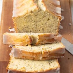 A sliced loaf of glazed lemon poppy seed bread on a cutting board.