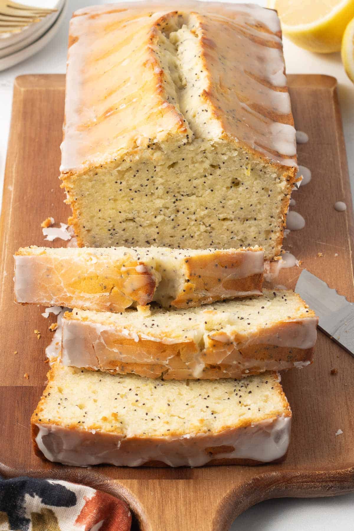 A sliced loaf of glazed lemon poppy seed bread on a cutting board.