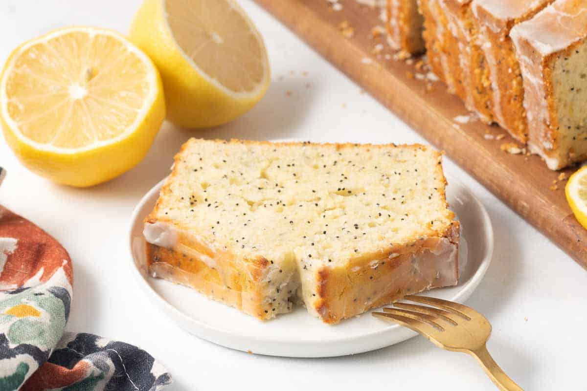 A slice of lemon poppy seed bread on a white plate with a fork.