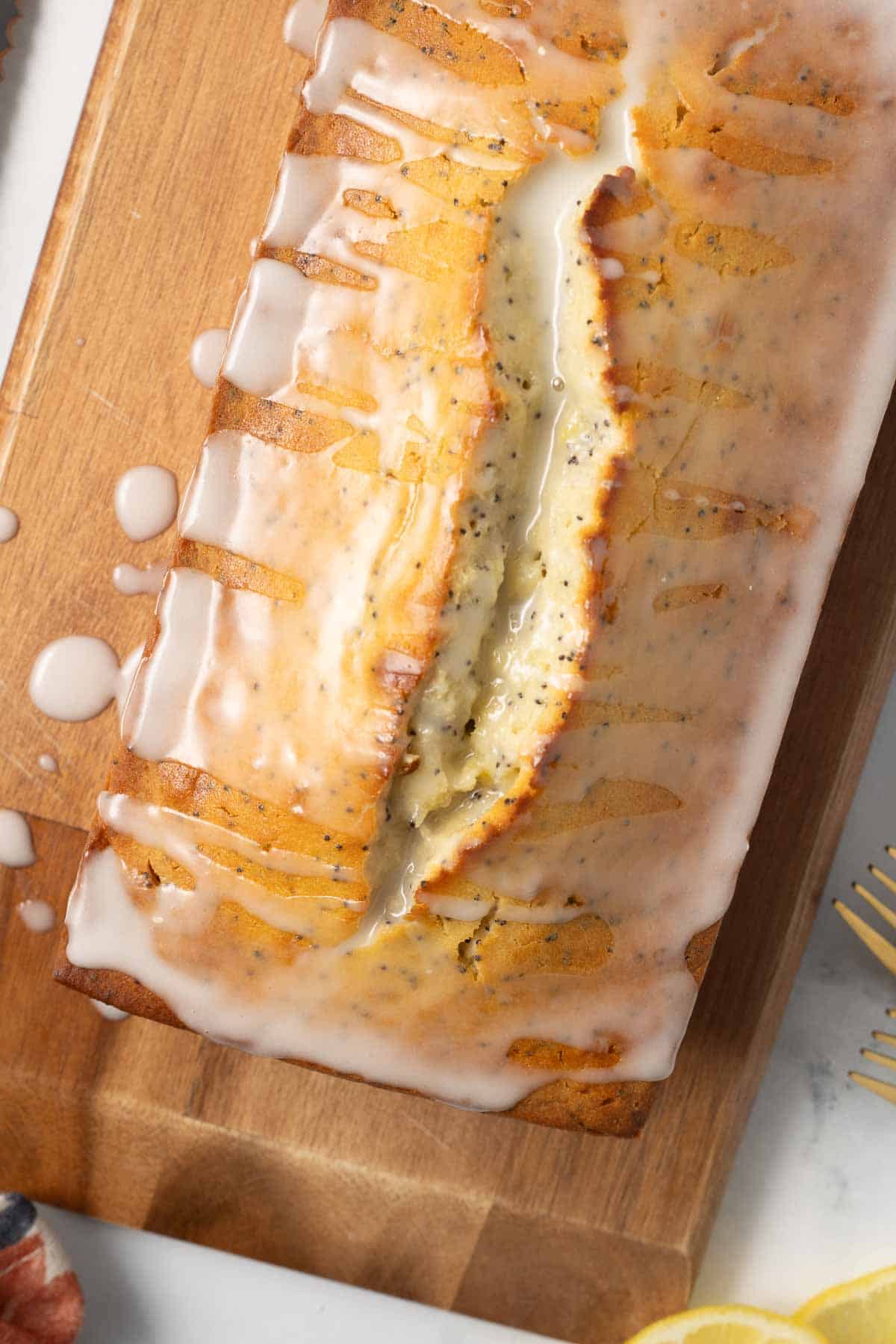 A loaf of glazed lemon poppy seed bread on a cutting board.